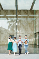 Sticker - Group of young people in protective masks standing at building wall outdoors and texting friends or checking social media