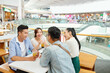 © DragonImages - Two couples sitting at cafe table in shopping mall, drinking tasty cocktails and discussing news