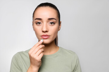 Canvas Print - Woman with herpes applying cream on lips against light grey background. Space for text