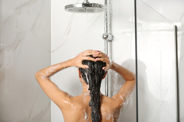 Canvas Print - Young woman washing hair in shower at home, back view