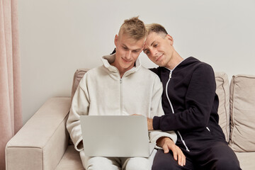 Two men lovers sitting at home in their pajamas communicate online, using a laptop. LGBT couple.