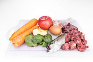 Ingredients of barf raw food recipe for dogs consisting meat, organs, fish, eggs and vegetable on chopping board