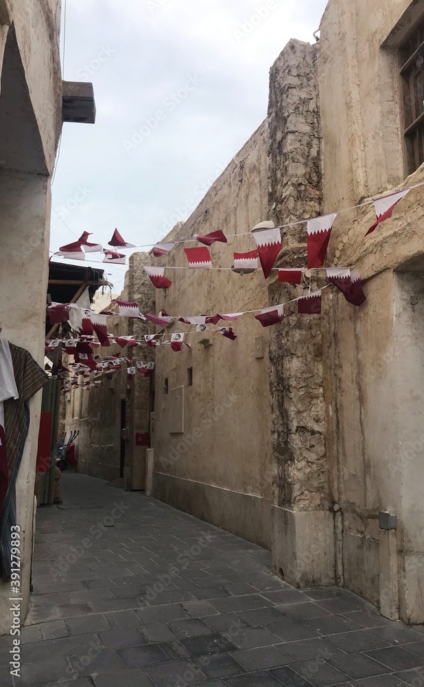 String of Qatari flags hanging between buildings on a windy day in Souq ...
