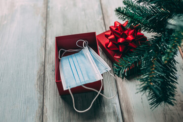 Face masks in red gift box under Christmas tree on wooden background. Covid-19 and holiday concept.