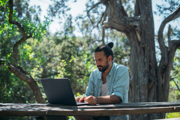 Male tourist working on a laptop outdoors in a camping.