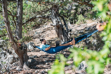 Wall Mural - A man works on a laptop while lying in a hammock