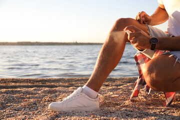 Man using insect repellent near sea on sunny day, closeup