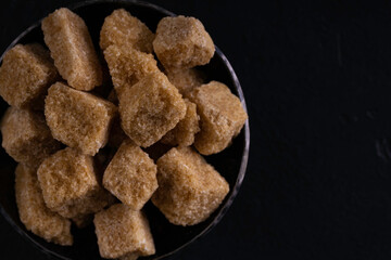 Natural brown sugar cubes in steel bowl on a dark background. Top view.