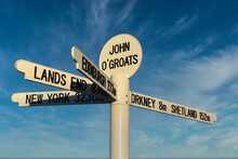 New John O'Groats Signpost On NC500 Route With Blue Sky And Light Cloud Background. Mileage To Orkney, Shetland, Lands End, Edinburgh And New York. Famous Spot For Tourists To Get Photographs Taken.