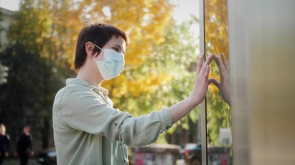 Woman in medical mask using interactive touchscreen display in the city, scrolling and touching. Entertainment and technology concept.