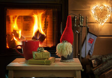 Mug Of Hot Chocolate Or Coffee, Gifts And Christmas Gnome On Vintage Wood Table In Front Of Fireplace As A Background.