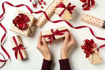 Woman holding Christmas gift box with red bow at white table, top view