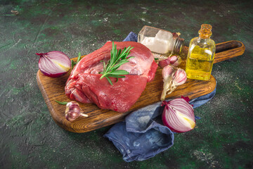 Wall Mural - Raw meat, beef fillet, large piece on a cutting board with spices for cooking. Black dark green background, copy space