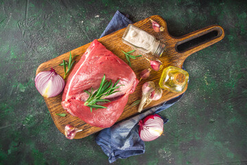 Wall Mural - Raw meat, beef fillet, large piece on a cutting board with spices for cooking. Black dark green background, copy space