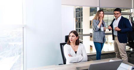 Turkish white collar woman is working on desk and there are two colleagues are gossiping at background behind of her