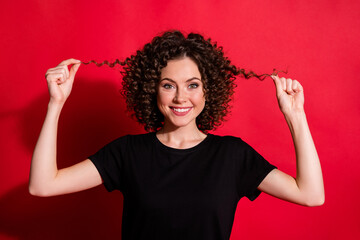 Sticker - Close-up portrait of lovely cheerful wavy-haired girl touching silky smooth hair isolated over bright red color background