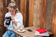 © Mint Images - Young blond woman sitting alone at a cafe table, looking at digital camera display.