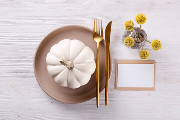 Thanksgiving table setting concept. Ceramic plate, fork and knife and mini pumpkin as traditional holiday symbol. Top view, close up, copy space, background.