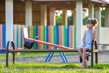 Canvas Print - Smiling cute young girl sitting alone outdoors on bench on sunny summer day.