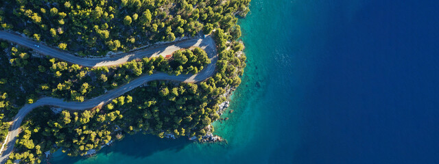 Wall Mural - Aerial drone ultra wide top down panoramic photo of curvy snake road crossing through vegetated tropical forest by the sea