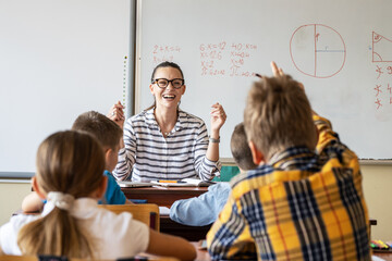 In the warm ambiance of the classroom, the kind female teacher engages in a lively discussion with her elementary school students, encouraging active participation and fostering a love for learning.