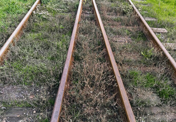 Old rusty, metal rails and wooden sleepers on a dirt surface with green grass. Railroad for passenger and freight trains. Photo, top view.