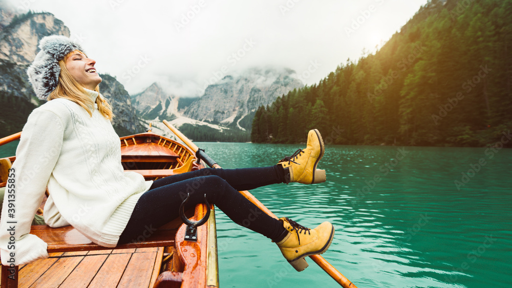 Tourist woman in traditional wooden rowing boat on italian alpine Braies Lake - Girl enjoying stunning view of Lago di Braies in Dolomites, South Tyrol, Italy, Europe. - obrazy, fototapety, plakaty 