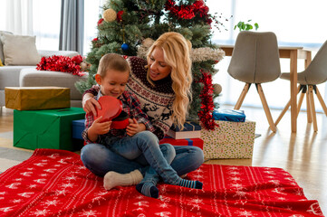 Cute little boy unboxing present with mother in front of Christmas tree. Christmas and holiday season concept