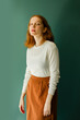 © Federica Giacomazzi/Stocksy - Portrait of a ginger girl in front of a green background wearing a white wool sweater and an orange skirt