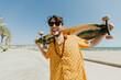 © Tadeu Dreyer/Stocksy - Young man with a longboard in front of the beach