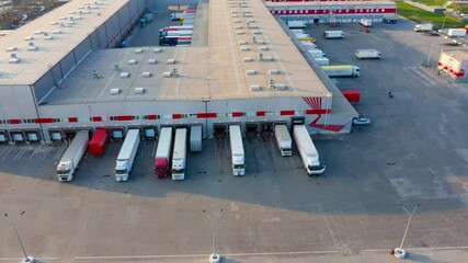 Wall Mural - Logistics park with a warehouse - loading hub. Semi-trucks with freight trailers standing at the ramps for loading/unloading goods at sunset. Aerial hyper lapse (motion time lapse)