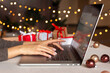 © Anna Voloshyna - Christmas shopping online, sales and discounts promotions during winter holidays, online shopping at home and lockdown coronavirus. Female hands on the laptop with gifts and blurred bokeh lights