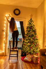 Woman hanging Christmas decorations above door entryway.