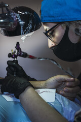 Wall Mural - Female tattoo artist tattooing a dragon on a man's arm