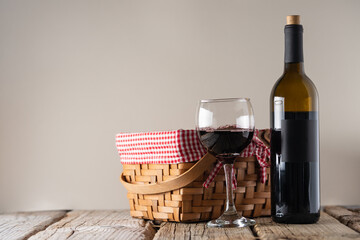 Bottle and glass with red wine with picnic basket on rustic wooden table on gray background. Concept of alcoholic drink. Photo for advertising and product promotion. Space for text.