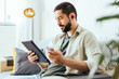 © kleberpicui - Young bearded man working from home. Man on sofa at home using digital tablet