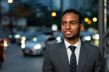 Wall Mural - Handsome African businessman outdoors at night smiling and thinking