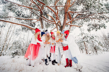 A large group of girls with tangerines are standing in the winter forest.Girls in red and white clothes with fruit in a snow-covered forest