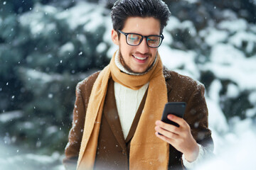 Sticker - Young man with phone in winter park.  Businessman uses a phone and  enjoying winter moments in a snowy forest. Snowfall.