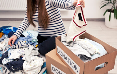 Wall Mural - Pregnant woman is sorting baby clothes and wanna give some things to charity