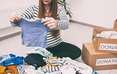 Wall Mural - Pregnant woman is sorting baby clothes and wanna give some things to charity