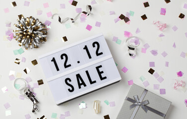 12.12 sale text on white lightbox, holiday ribbon and box around on white background.