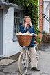 © Mint Images - Young blond woman on bicycle with basket, talking on mobile phone.