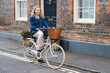 © Mint Images - Young blond woman cycling down a village street.