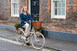 © Mint Images - Young blond woman cycling down a village street.