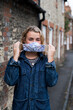 © Mint Images - Young blond woman standing outdoors, putting on face mask.