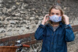 © Mint Images - Young blond woman standing outdoors, putting on face mask.