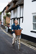 © Mint Images - Young blond woman cycling down a village street.