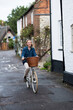 © Mint Images - Young blond woman cycling down a village street.