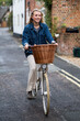 © Mint Images - Young blond woman cycling down a village street.